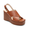 The Sanctuary Clothing "Nouveau Luggage" features a brown wedge with crossover straps, open toe, textured platform heel, and adjustable slingback buckle.