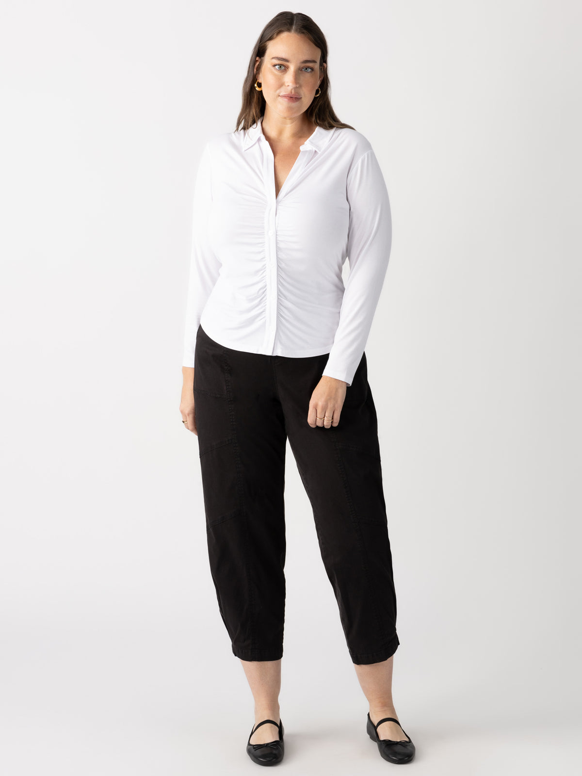 A woman in Sanctuary Clothing's "dreamgirl button up white" long-sleeve blouse and black pants stands against a plain backdrop. She has long brown hair and wears black flat shoes.