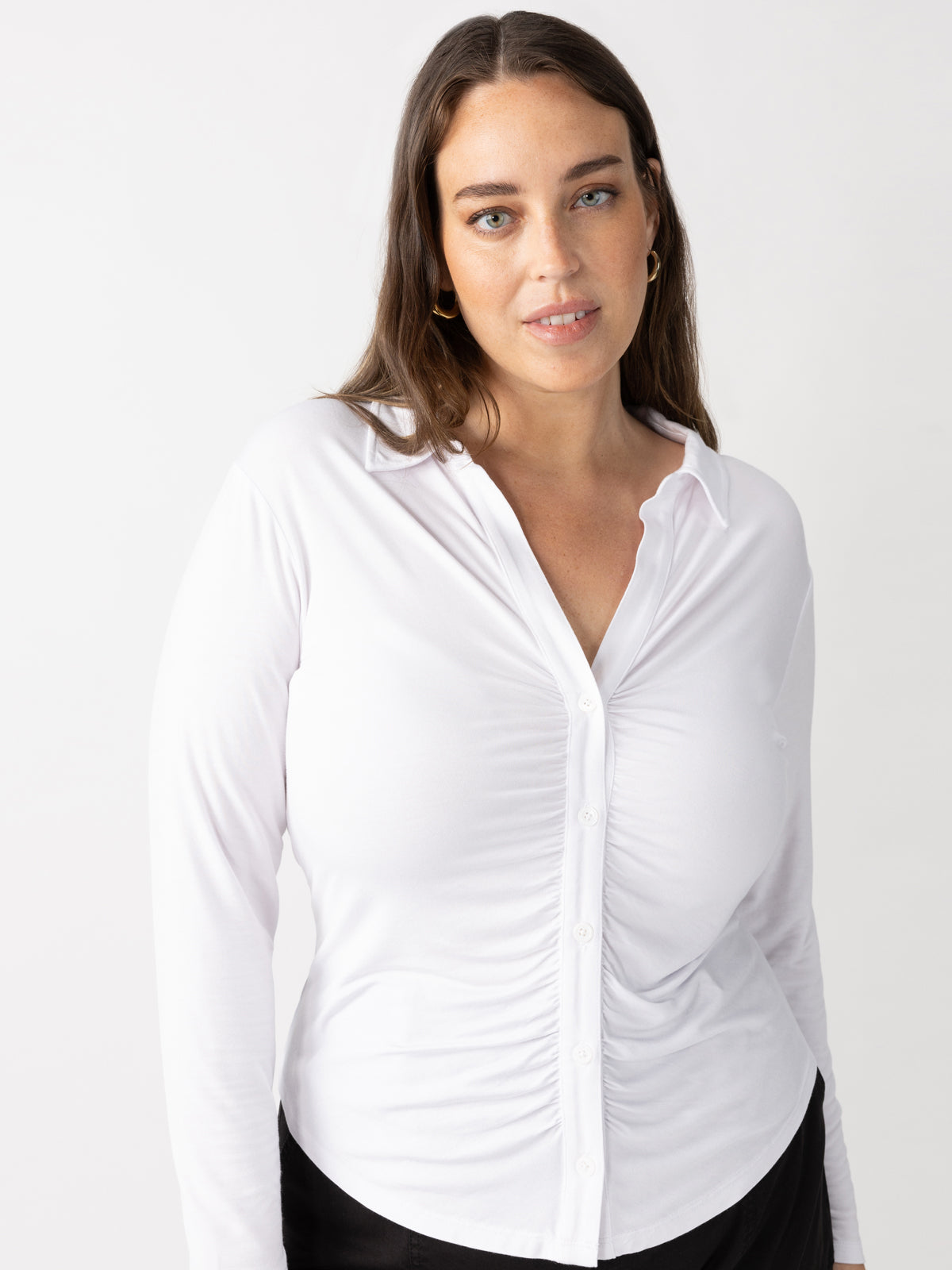 A person with long dark hair is wearing the "dreamgirl button up white" by Sanctuary Clothing and black pants, looking at the camera against a plain white background.