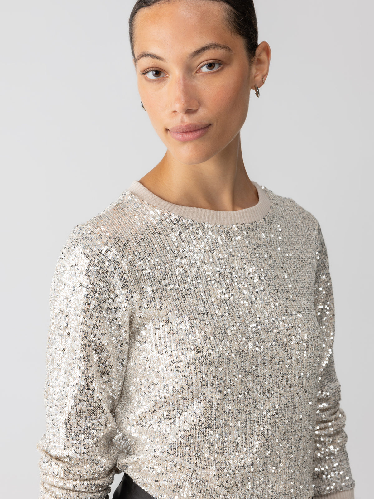 A person with short, dark hair is wearing the Sparkle Together Top in Champagne by Sanctuary Clothing and small hoop earrings, standing against a plain white background. They have a subtle smile and are looking towards the camera.