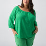 A woman with long dark hair wearing the Beach To Bar Blouse Green Goddess Inclusive Collection by Sanctuary Clothing, tucked into green cargo pants, stands against a plain white background. She is looking slightly to the side with her hands in her pockets.