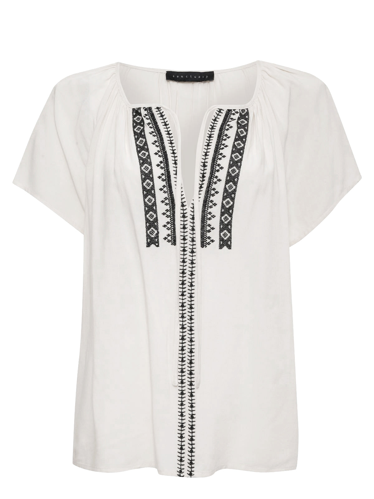 The Golden Dream Top Birch by Sanctuary Clothing is a light-colored short-sleeve blouse adorned with black embroidered patterns along the center and neckline. It has a loose, comfortable fit and features a rounded neckline with gathered fabric at the shoulders.