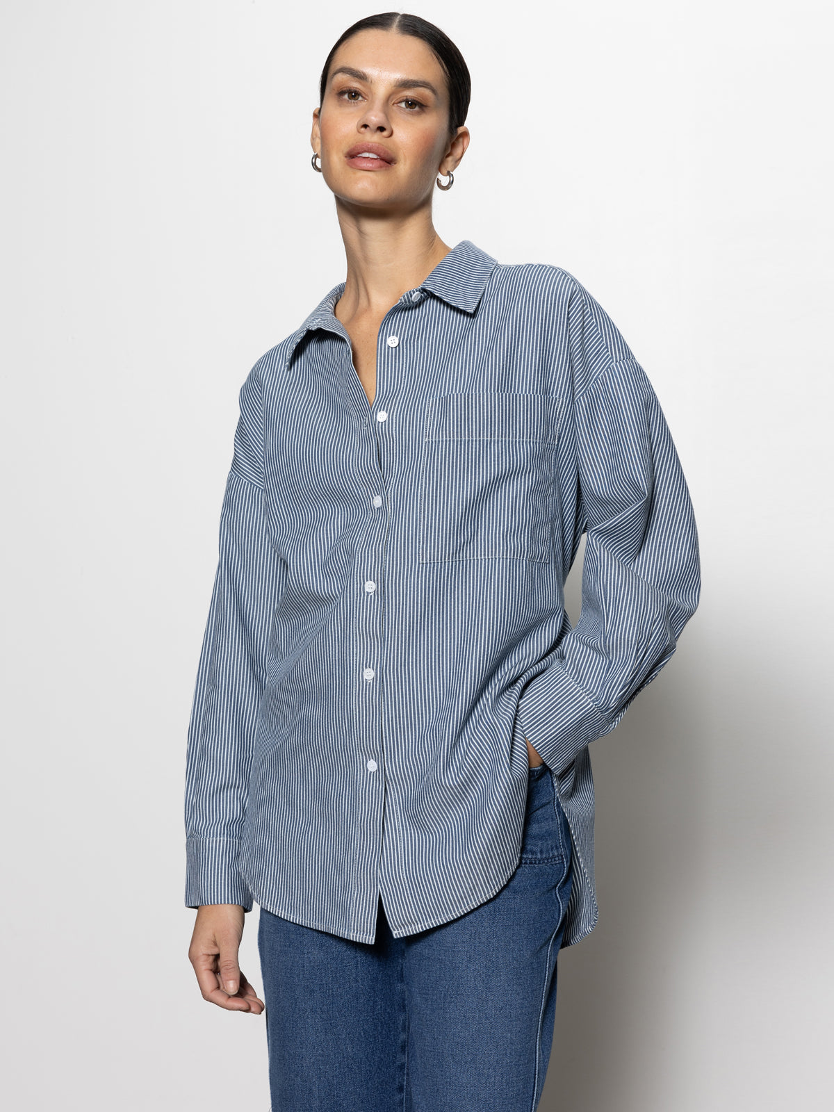 A person wearing Sanctuary Clothing's "boyfriend tie back shirt" in marina stripe and blue jeans stands against a plain white background. They have their dark hair pulled back and look directly at the camera.