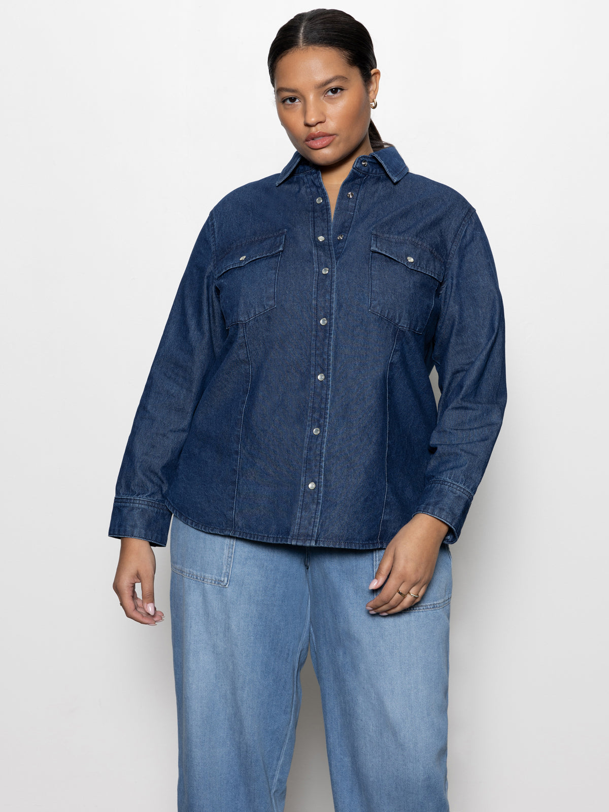 A person wearing the Denim Western Shirt from Sanctuary Clothing’s Inclusive Collection in blue slate and light denim pants stands against a plain white background.