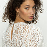 A woman with curly hair is wearing the cherished lace tee in white by Sanctuary Clothing, looking over her shoulder against a plain background.