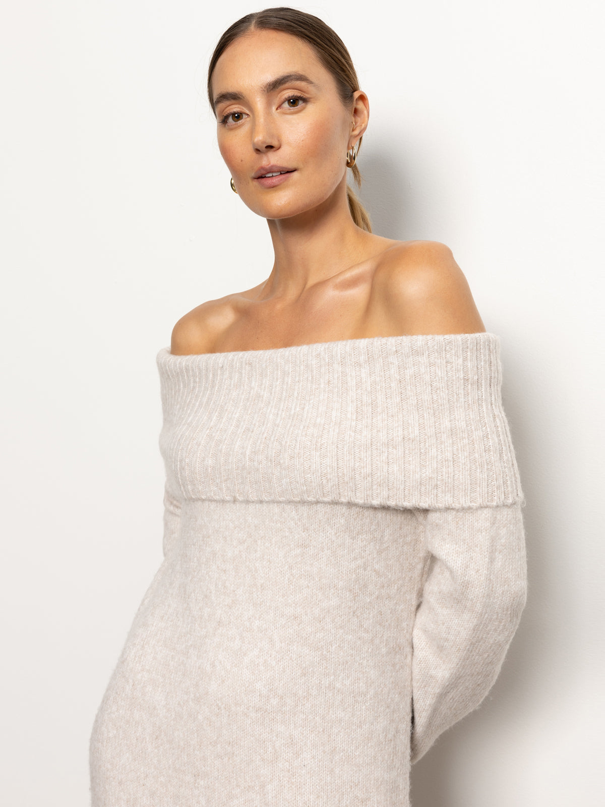 A person with tied-back hair is wearing the "off shoulder dress coconut smoke" by Sanctuary Clothing. They are standing against a plain white background, looking directly at the camera with a neutral expression.