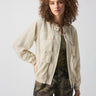 A person with curly hair is wearing the Field Utility Jacket Birch from Sanctuary Clothing over an olive green top and camo-patterned pants. They are standing against a plain white background.