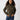 A woman with long curly hair wears the Corduroy Surplus Bomber in Burnt Olive by Sanctuary Clothing paired with blue jeans. She stands against a plain, light-colored background, looking confidently at the camera with her hands in her jacket pockets.