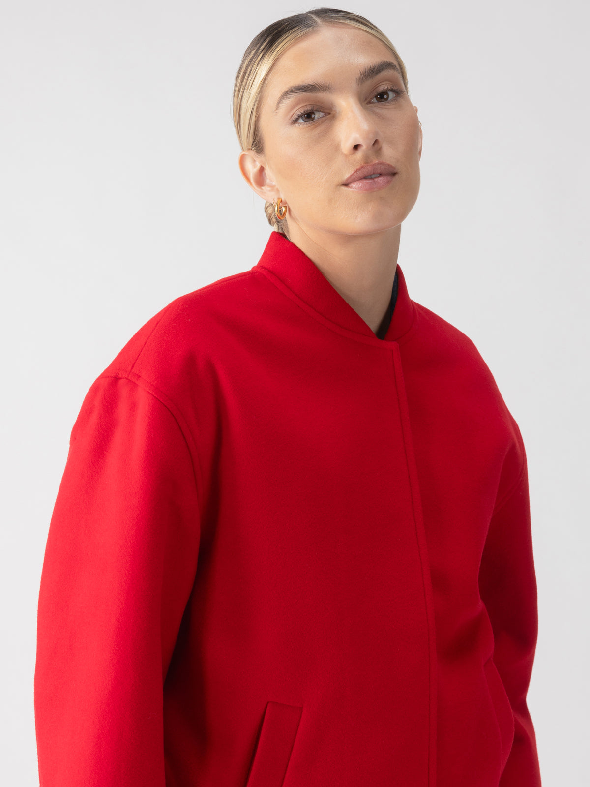 A person wearing the Modern Bomber Jacket in Mars Red by Sanctuary Clothing stands against a plain background. They have their hair styled in a sleek updo and are sporting gold hoop earrings.