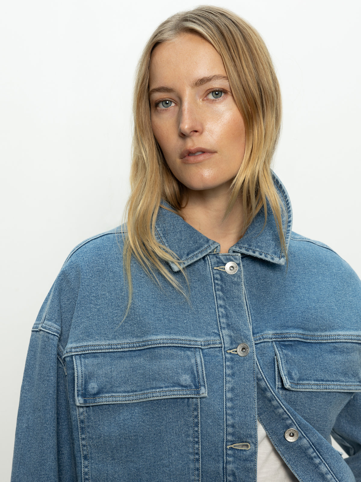 A person with long blonde hair wearing the Sanctuary Clothing "Make Way Denim Jacket Wayfarer" looks directly at the camera against a plain background. The jacket features button details and chest pockets.