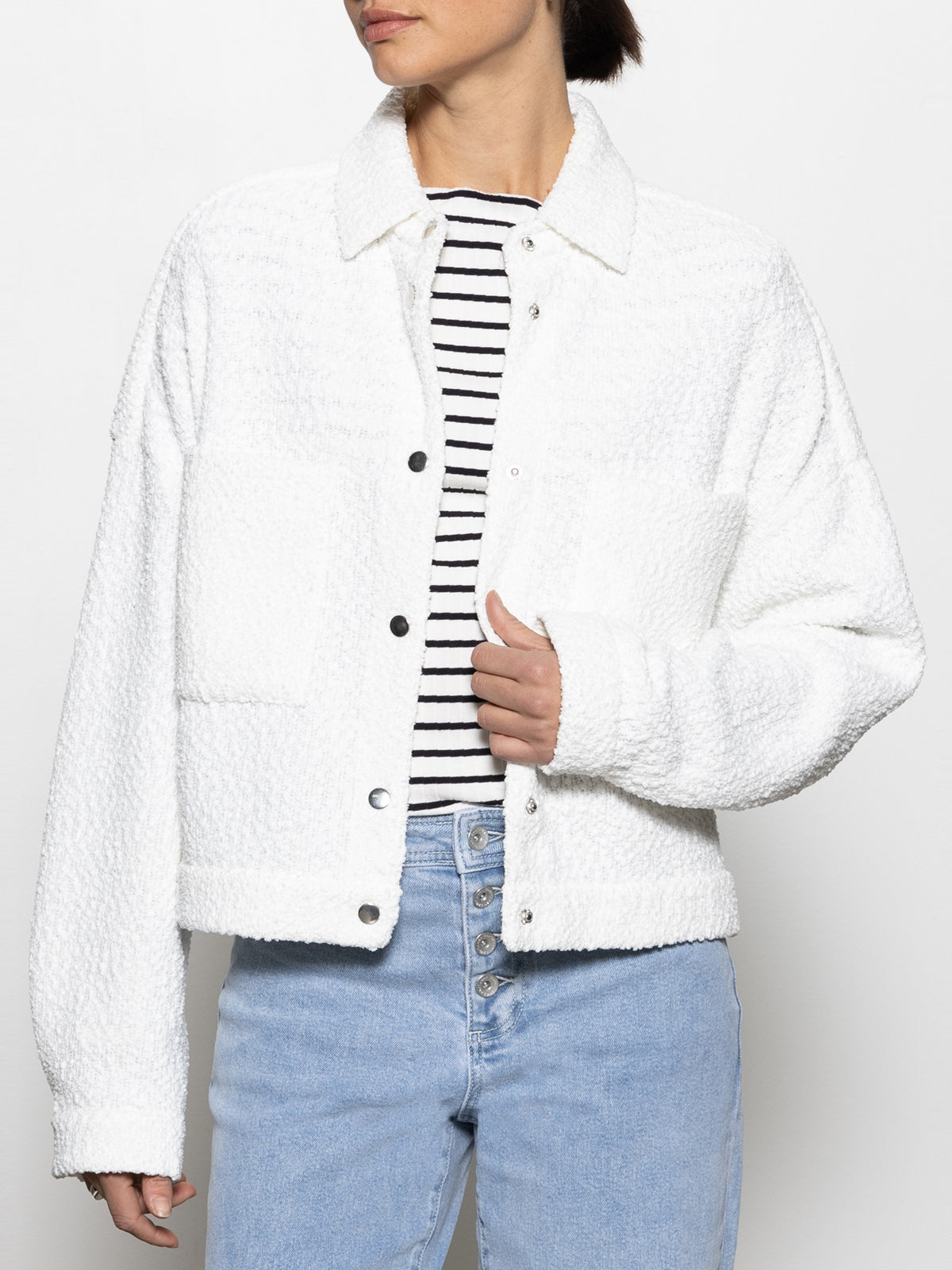 A person wears the Sanctuary Clothing "Trimmer Knit Shacket Chalk" featuring a textured design, large front pockets, and metal buttons over a black and white striped shirt with light blue jeans against a plain white background.