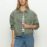 Person in a Sanctuary Clothing coastal denim shacket in dark spruce over a striped shirt and blue jeans, standing against a plain background with relaxed hands, looking forward.