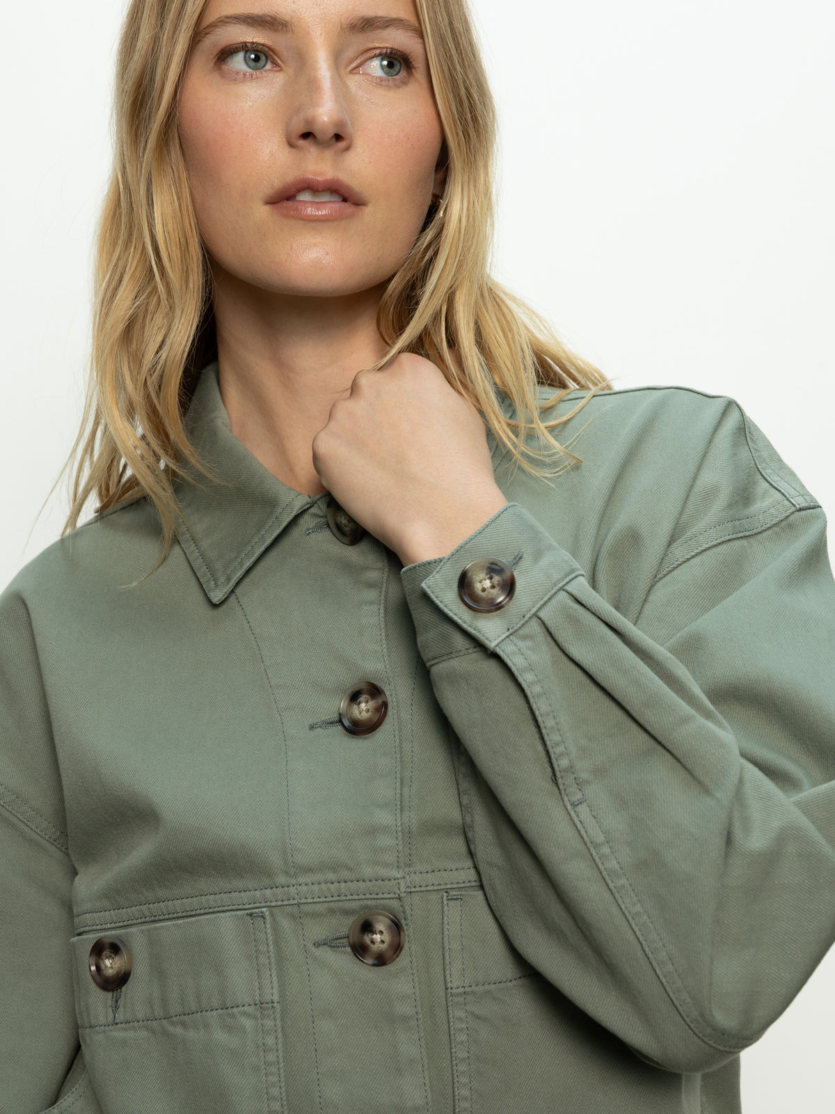 A woman with long blonde hair models the Sanctuary Clothing coastal denim shacket in dark spruce, standing against a plain background and gazing slightly upward.