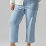 A person wearing the Sanctuary Clothing Vacation Crop Pant Ultra Pale from the Inclusive Collection, a high-waisted, wide-leg design with large front pockets, paired with a white textured cardigan and open-toed beige block-heeled sandals. The photo captures the individual from the chest down to showcase the garments and shoes.