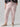 Person wearing Rebel Pant Washed Pink No 3 Inclusive Collection by Sanctuary Clothing with ankle cuffs and a black sweater featuring light pink flowers. They are also wearing beige ballet flats. The person's hands are in the pants' pockets. The background is plain and light gray.