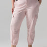 Person wearing Rebel Pant Washed Pink No 3 Inclusive Collection by Sanctuary Clothing with ankle cuffs and a black sweater featuring light pink flowers. They are also wearing beige ballet flats. The person's hands are in the pants' pockets. The background is plain and light gray.