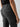 A close-up shot of a person wearing the Rebel Pant Obsidian by Sanctuary Clothing, featuring the back pocket and part of the leg with a side pocket. The person is also wearing a black shirt, and one hand is resting by their side.