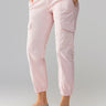 A person is dressed in Sanctuary Clothing's Rebel Pant Washed Pink No 3, featuring side pockets and gathered ankles. They are also wearing a light-colored knit sweater paired with metallic silver ballet flats. With their hands tucked into the pockets, they pose against a neutral background.