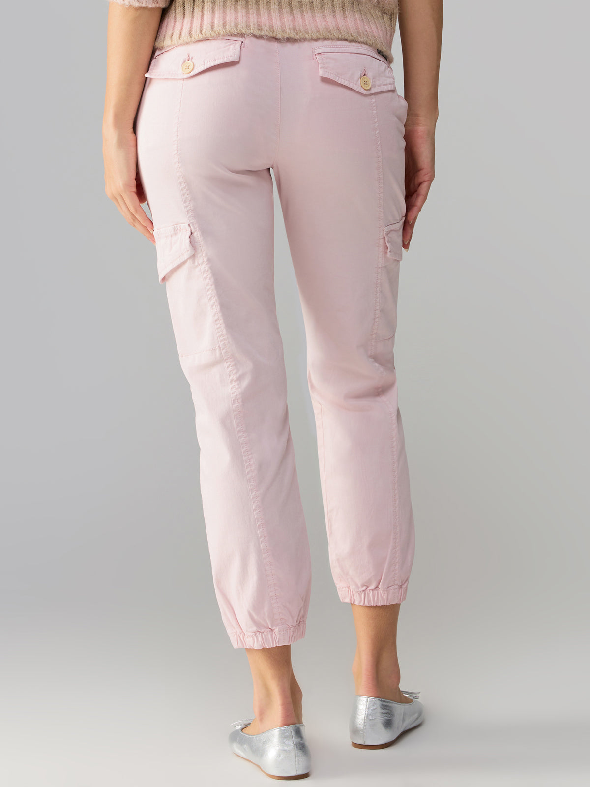 A person is wearing the Rebel Pant Washed Pink No 3 from Sanctuary Clothing, which features flap pockets on the back and sides. They are also wearing light-colored, flat shoes against a plain, light gray background.