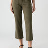 A person models the "Vacation Crop Burnt Olive" pants by Sanctuary Clothing, which feature large front pockets. They are pairing the olive green cropped pants with a black top and black strappy flat sandals. The background is a plain, light color, showing only their lower torso and legs.