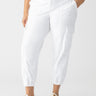 A person is wearing the Rebel Pant Eco Natural Inclusive Collection from Sanctuary Clothing, showcasing a stylish look with hands in pockets, button and zipper closure, and side pocket details. They are also pairing the pants with white sneakers featuring beige stripes and a patterned top in shades of blue, white, and black.