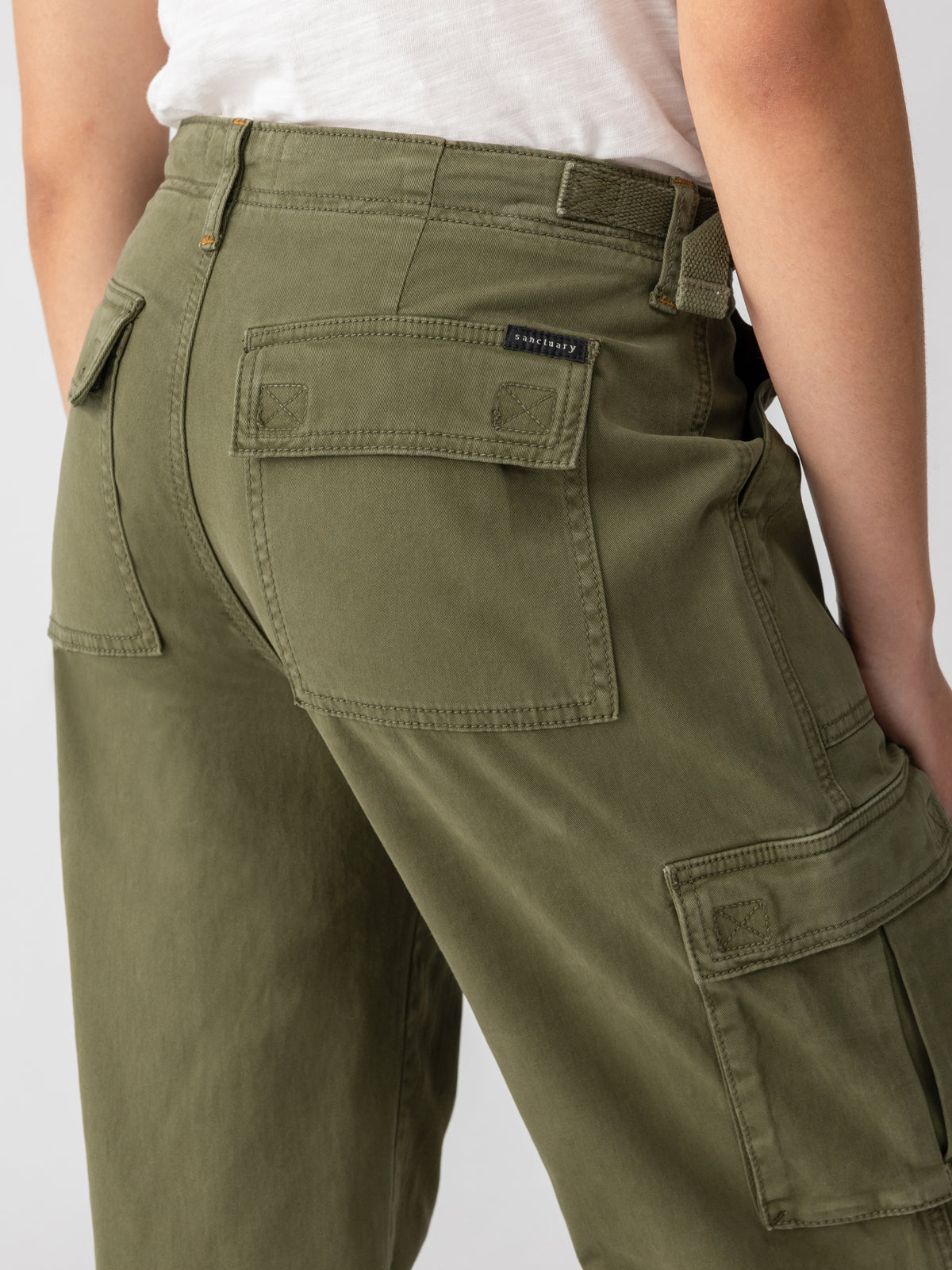 Close-up of a person wearing Sanctuary Clothing's Reissue Cargo Pant in Mossy Green. The image shows the back view, highlighting the pants' large back pockets and side pockets, along with a part of a white shirt tucked in. The person is standing against a plain background.