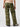 A person is standing with their back to the camera, wearing the Sanctuary Clothing Reissue Cargo Pant Renew Camo, which features green camouflage and large side pockets. They are also sporting a light-colored sweater and white shoes. The background is plain and white.