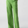 A person is wearing Sanctuary Clothing's Reissue Cargo Washed Chlorophyl, which are bright green cargo pants that feature side pockets and a button closure. They are also sporting black sandals with white soles. The image highlights the lower half of the individual against a plain white background.