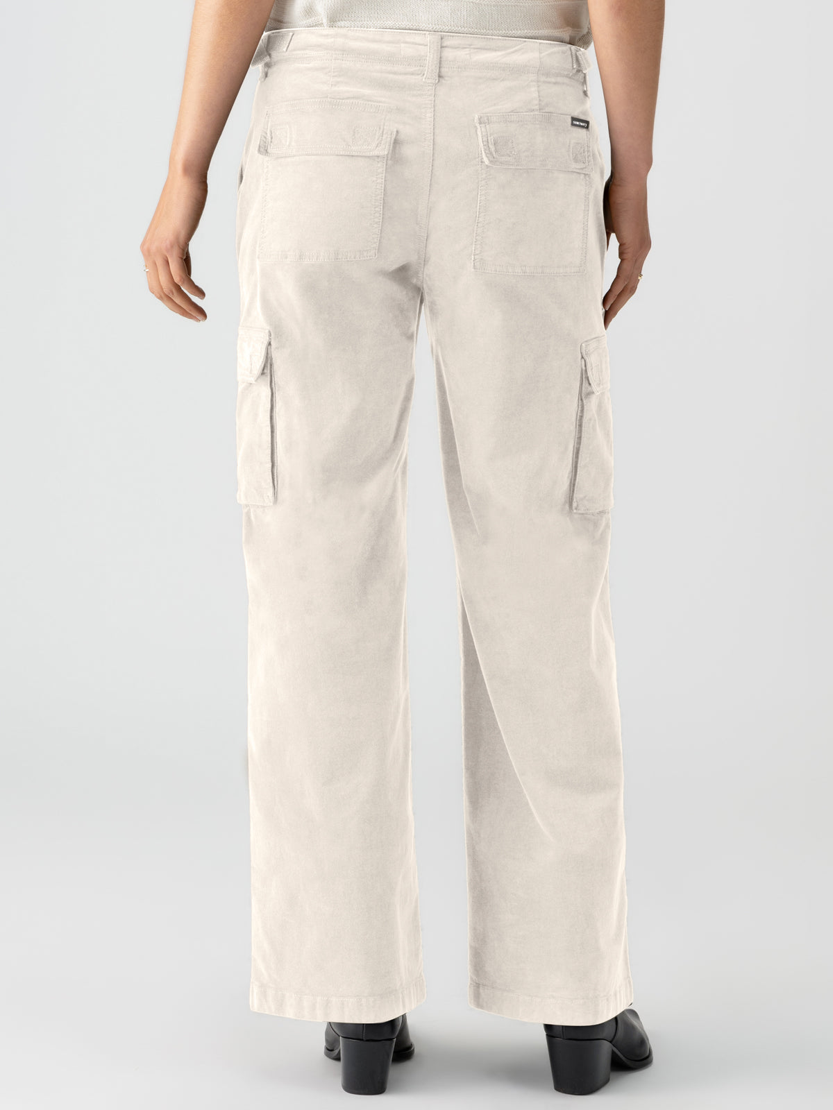 A person, seen from behind, is wearing the Sanctuary Clothing Reissue Cargo Toasted Almond wide-leg cargo pants, featuring two back pockets and two side cargo pockets. They are also dressed in black shoes and a light-colored top against a plain, light grey background.