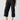 A person is wearing the Cali Cargo Pant Black by Sanctuary Clothing, featuring multiple pockets and rolled up to mid-calf length. They are also sporting black ankle-strap sandals, with a partially visible white top. The background is plain and light-colored.