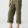 Person wearing Sanctuary Clothing's Cali Cargo Pant in Mossy Green, which features multiple pockets and rolled-up cuffs, paired with tan flat sandals. The person’s hand is resting in their pocket, and they are standing against a plain background. Only the lower half of the body is visible.