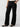 A person is wearing Low Slung Y2K Pant Black from Sanctuary Clothing, which features a straight fit and multiple pockets. They have one hand in a pocket and are posed against a plain light-gray background. The person is also wearing black ballet flats and a white top with a faint pattern.