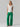 A woman with long blonde hair stands confidently against a neutral background. She is wearing a simple white t-shirt and the Low Slung Y2K Pant Jelly Bean from Sanctuary Clothing, bright green cargo pants with multiple pockets. She has one hand in her pocket and the other hanging by her side.