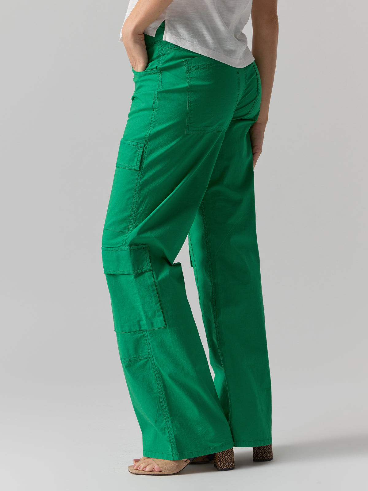 A person wearing the "Low Slung Y2K Pant Jelly Bean" by Sanctuary Clothing and a white top is shown from the waist down. The pants feature multiple pockets and a loose fit. The individual is also sporting tan, open-toe block heels against a neutral gray background.