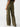 A person is wearing the Low Slung Y2K Mossy Green cargo pants by Sanctuary Clothing. These high-waisted pants, featuring large pockets on the back and sides, are wide-legged and paired with a black top. The background is plain and white.