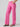 A person is wearing the Low Slung Y2K Wild Pink cargo pants by Sanctuary Clothing, paired with a white top. They are standing with one hand in their pocket and their feet slightly apart, sporting black sandals with a gold buckle against a plain gray background.