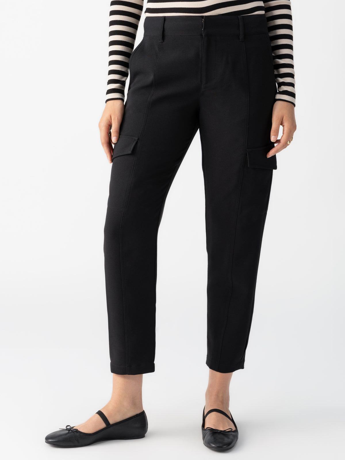 A person wearing a black and white striped long-sleeve top, Sanctuary Clothing's Polished Cargo Pant in Black featuring side pockets, and black ballet flats. The photo is taken against a plain white background, showing from the torso down to the feet.