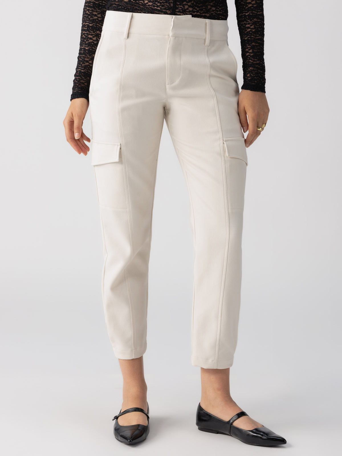 A person is wearing the Polished Cargo Pant in Toasted Marshmallow by Sanctuary Clothing, paired with a black, long-sleeved lace top. The outfit is completed with black, pointed-toe flats. Only the lower half of the person's body is visible against a plain background.