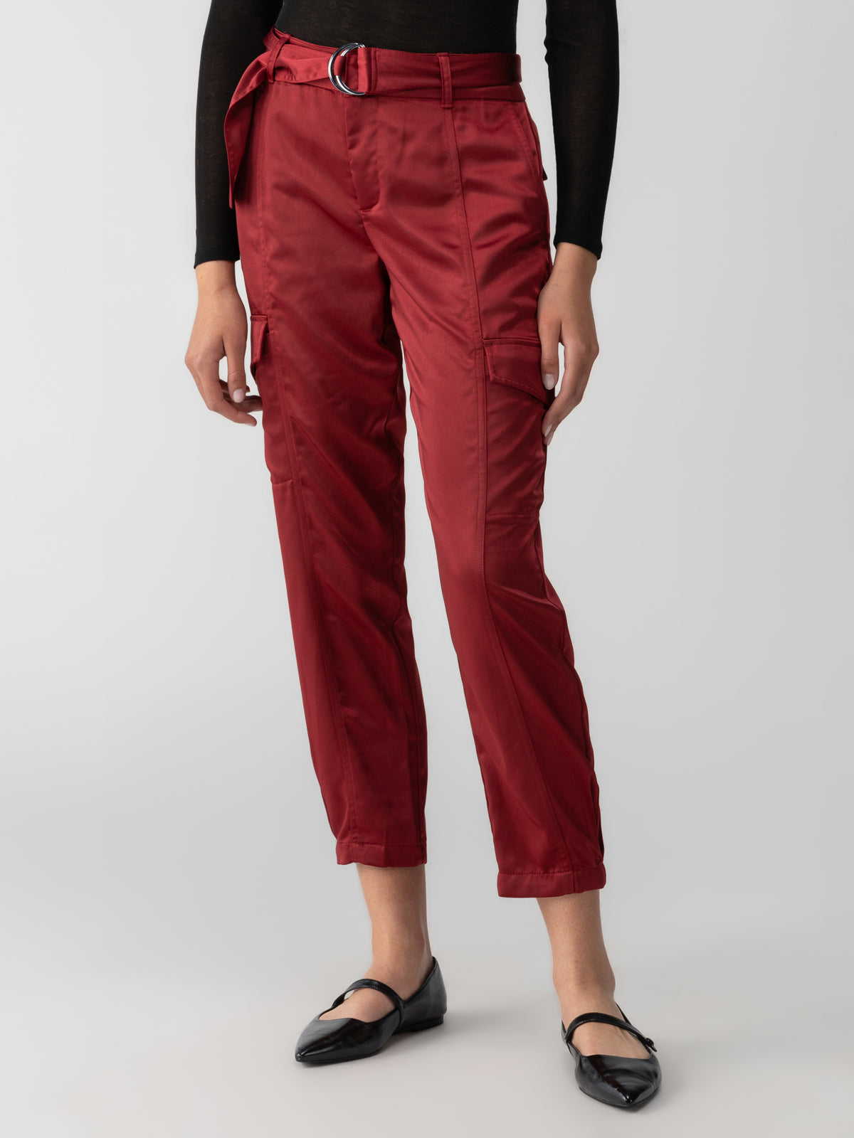 A person stands against a plain background wearing the Classy Cargo Trouser Garnet by Sanctuary Clothing, paired with a matching belt. They are also wearing a black long-sleeved top and black flat shoes with buckles. The photo is cropped to show only the body from the shoulders down.