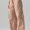 A person wearing Sanctuary Clothing's Cargo Parachute Pant Bare Nude, which are loose-fitting with multiple large leg pockets and an elastic waistband with a drawstring. They are posing with one hand in a pocket, wearing a white top and beige shoes against a plain gray background.