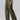 A person is dressed in Sanctuary Clothing's Cargo Parachute Pant Renew Camo, a green camouflage cargo pant with a loose fit and multiple side pockets. They are also wearing brown sandals and a black top. The background is plain gray, showing only the lower half of their body.