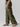 The photo features a person wearing the Cargo Parachute Pant Renew Camo by Sanctuary Clothing and brown sandals. Captured from a side view, the image shows the lower half of their body adorned in loose-fitting, green camouflage cargo pants with multiple pockets. A black top is partly visible in the shot against a plain gray background.