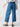 A person wearing the Sanctuary Clothing Reissue 90S Sash Spring Valley wide-leg, high-waisted blue jeans with buttoned back pockets and a white blouse. They're standing on a light gray background with their back to the camera and their left arm slightly bent. They're also wearing black sandals.