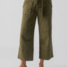 A person is wearing the "Reissue 90S Sash Burnt Olive" high-waisted, wide-leg pants from Sanctuary Clothing, which feature a tied waist belt, large front pockets, and visible seam details. They are also wearing a white top and brown sandals against a plain white background.