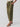 A person is wearing the Reissue 90S Sash Burnt Olive cargo pants from Sanctuary Clothing, featuring large front pockets and a fabric tie belt. They are also sporting a light-colored top and tan sandals. The photo captures them from the waist down against a plain background.