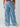 A person is standing, wearing the Sunset Denim Pant in Pale Blue from Sanctuary Clothing's Inclusive Collection, which are wide-leg cargo jeans with front and side cargo pockets. Their partially visible top features a floral pattern, and they are also wearing beige shoes. The background is plain white.