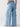 A person is shown from the back, wearing the Sanctuary Clothing Sunset Denim Pant in Pale Blue, which features wide-legs and large side pockets. They are also wearing a light-colored top tucked into the jeans. The background is plain white.