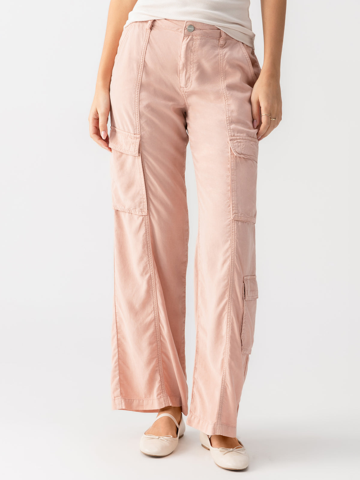 A person wearing the Sanctuary Clothing Doheny Cargo Smokey Rose pants and a white top stands against a plain white background. The pants feature multiple pockets, and the person is also wearing light-colored flat shoes.