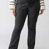 A person stands wearing Sanctuary Clothing's Sculpted Hayden Bootcut Black Inclusive Collection pants, which feature front and side pockets, paired with a white sweater adorned with black horizontal stripes. The person’s feet are in black flat shoes, and the background is a plain light gray.