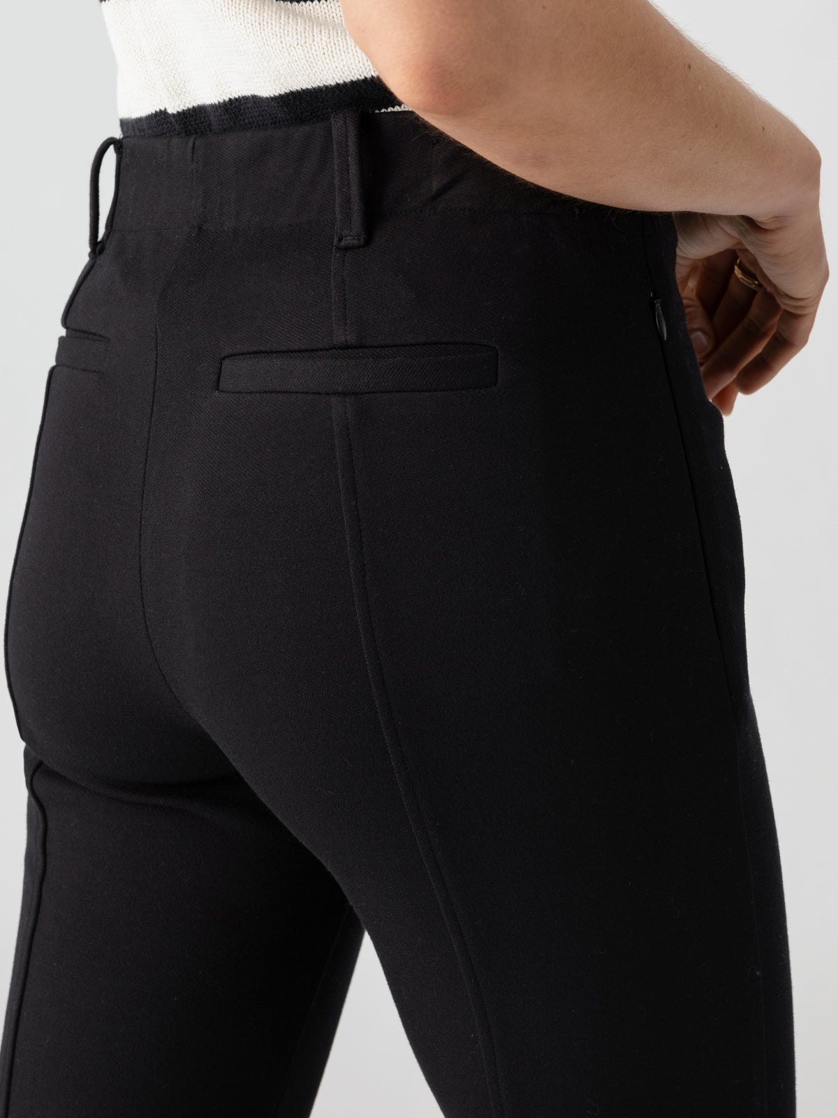 A person wearing the Cassie Legging Black by Sanctuary Clothing poses with their right hand resting on their hip. The side and back of the leggings are visible, emphasizing their fit. The person is also wearing a white top.